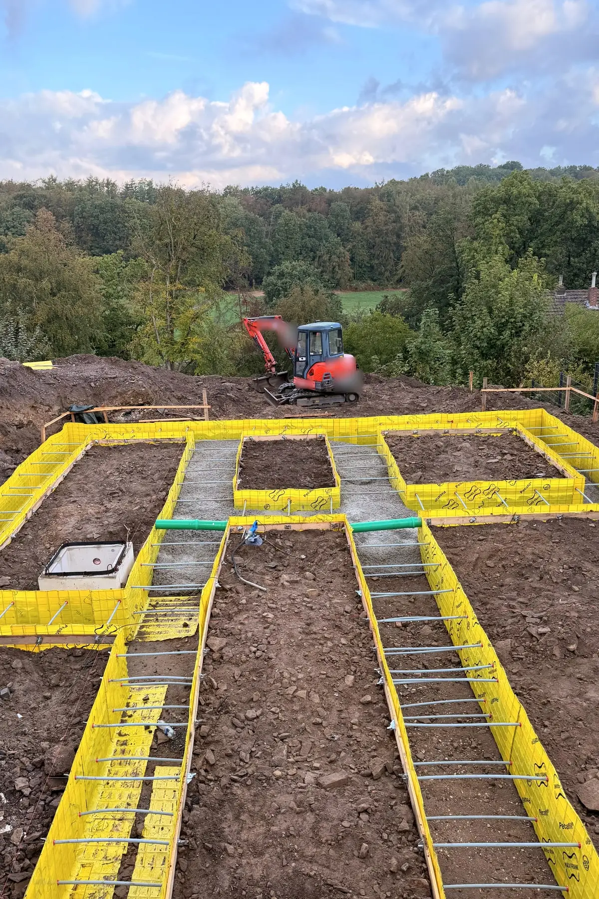 Neubau: gelbe Schalung für die Fundamente, im Hintergrund ein Minibagger